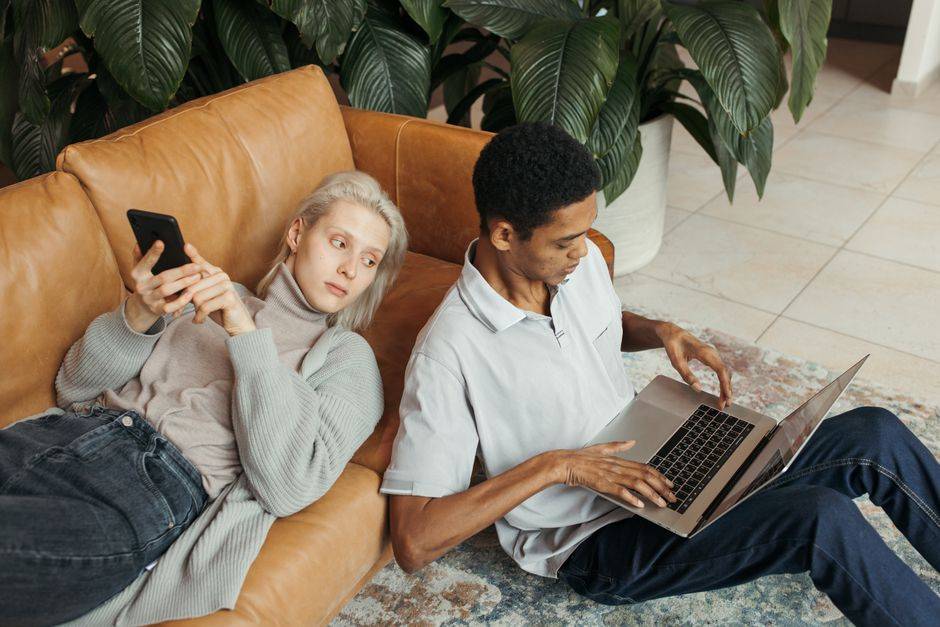 Couple relaxing on sofa, woman using smartphone, man working on laptop, VPN security and digital