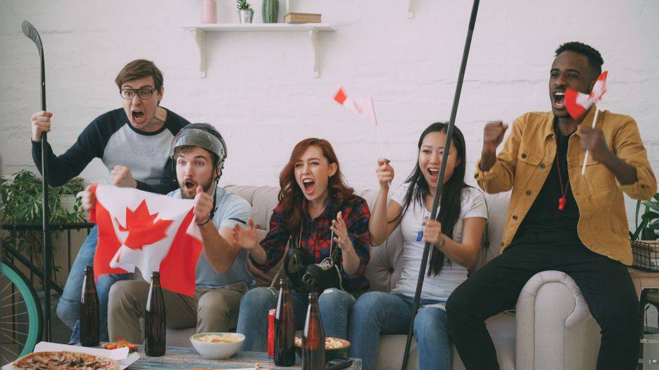 Group of friends celebrating with Canadian flags and hockey sticks, bypassing geo-restrictions for NHL TV.